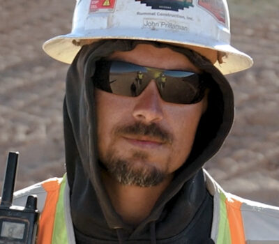 Employee-owner John Prillaman wearing a white hard hat, black sunglasses, and a black hooded sweatshirt.