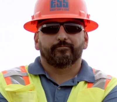 Headshot of male construction worker wearing an orange hard hat and high visibility safety vest.