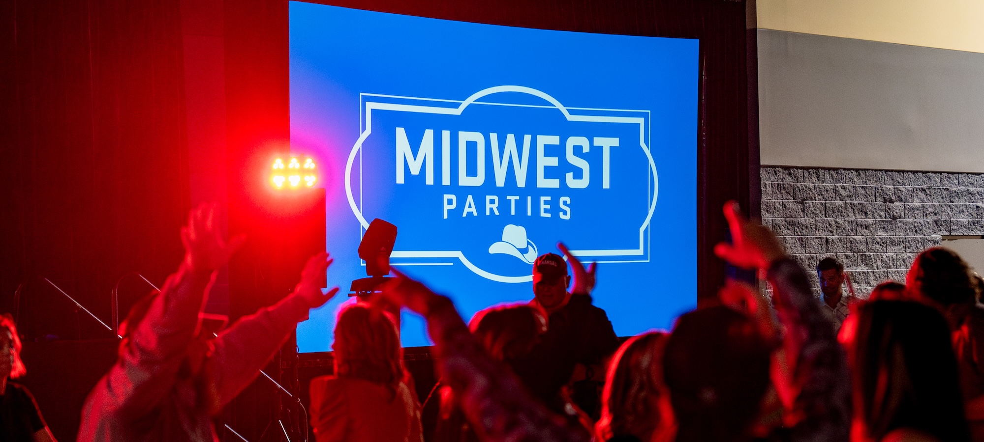 A crowd has their hands in the air in front of a presentation screen that reads 