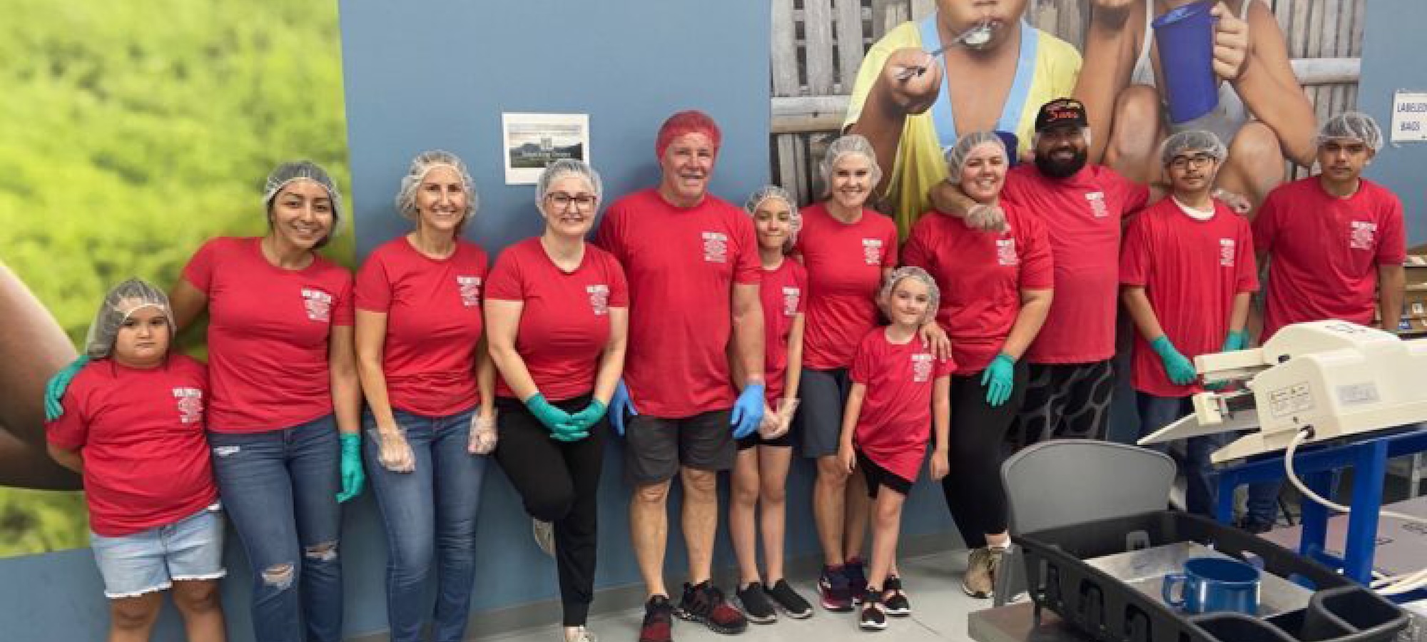 A group in red shirts and hair nets pose at a community service event.