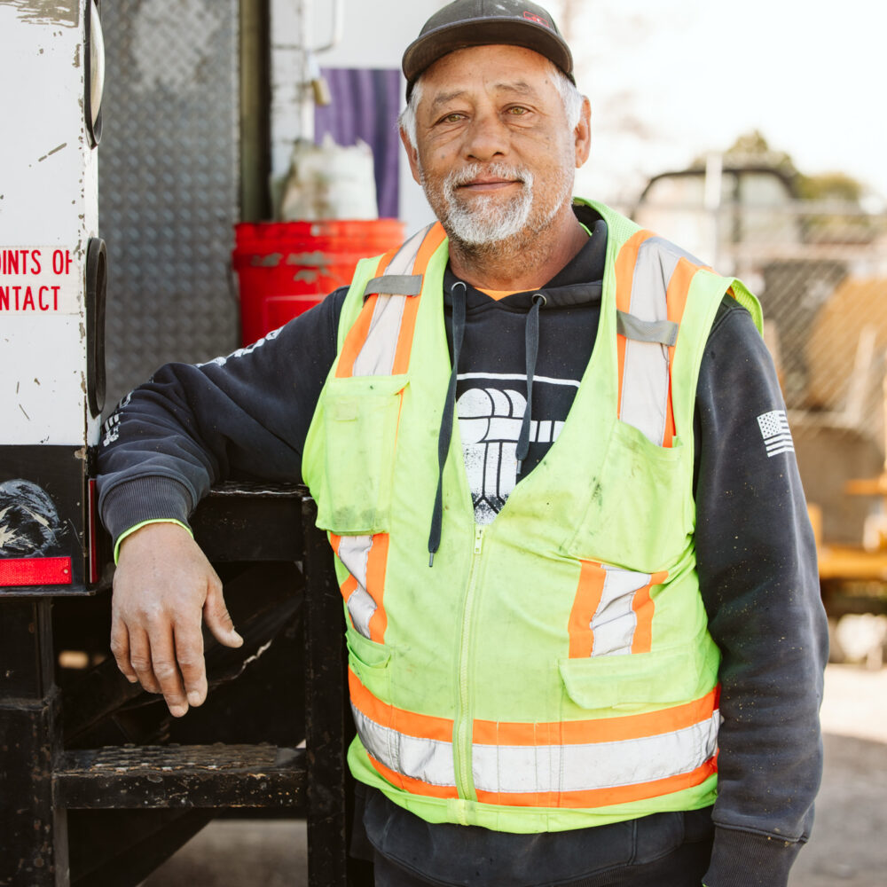 A construction worker poses with his arm resting on a truck.