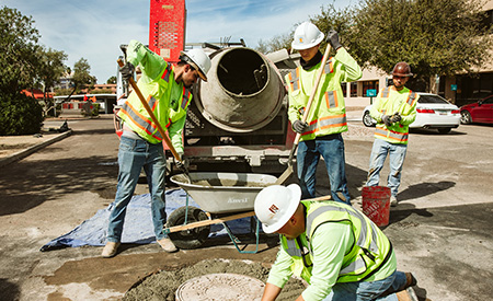 A construction crew shovels material out of a wheelbarrow while working in the street.