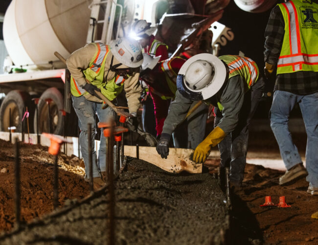 nighttime view of construction works bending over to level concrete on a jobsite