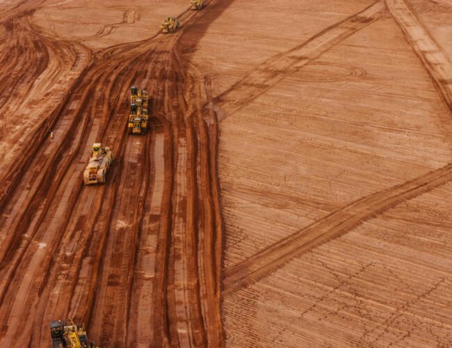 aerial view showing heavy civil construction equipment on an excavation site with red-orange dirt